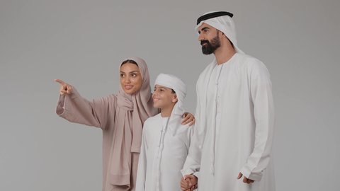 مفهوم الترابط الأسري، مشاركة الأوقات الممتعة مع الأبناء، بورتريه لام عربيه خليجيه اماراتية ترتدي العباءه الملونه تقوم بقضاء وقت ممتع برفقه زوجها و ابنها بايماءات السعادة و السرور، الاشارة بإصبع السبابة إلى شيء محدد