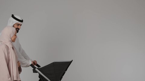 Emotional bonding, side portrait of an Emirati Gulf Arab man pulling a stroller with his wife, happy family concept, family outing and tour, spending quality time with family