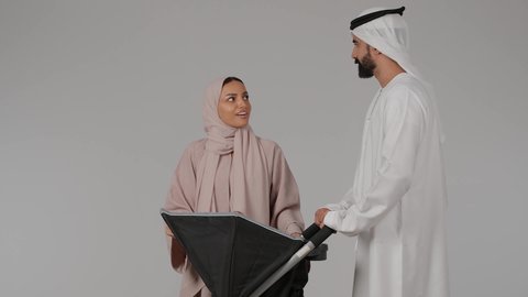 مفهوم الأمومة والرعايه والاهتمام بالأولاد،عائلة اماراتية تقضي اوقات ممتعة، بورتريه لام عربيه خليجيه اماراتية ترتدي العباءه الملونه برفقه زوجها تنظر الى إبنها الرضيع داخل العربة و تلعب معه بسعادة بإيماءات تدل على الحب والأمان