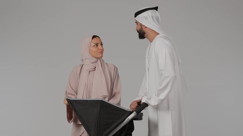 أهمية الأهل ودورهم الأساسي في تربية ونشأة الأبناء، عائلة اماراتية تقضي اوقات ممتعة، بورتريه لام عربيه خليجيه اماراتية ترتدي العباءه الملونه برفقه زوجها تنظر الى إبنها الرضيع داخل العربة و تلعب معه بسعادة بإيماءات تدل على الحب والأمان