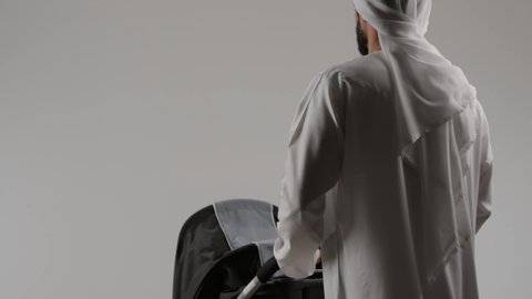 الرعاية والاهتمام بالأبناء، مفهوم الرابطة الأبوية, إيماءات الحب والعطف على الأبناء، بورتريه من الخلف لأب عربي خليجي اماراتي يرتدي الكندورة و الغتره يقوم بجرعربه الاطفال ، خلفية رمادية