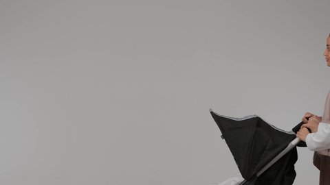 مفهوم الأسرة السعيدة، نزهة و جولة عائلية ، المشي والتنزه برفقة الأسرة، بورتريه لسيدة عربية خليجية اماراتية ترتدي العباءة الملونه تجر عربة الاطفال برفقة ابنها بإيماءات تدل على السعادة و المحبة و الحنان