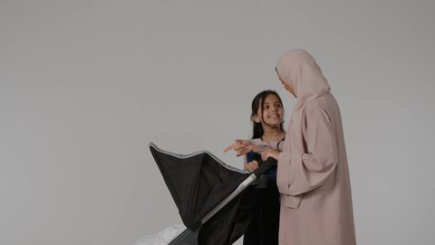 نزهة و جولة عائلية ، المشي والتنزه برفقة الأسرة، بورتريه لسيدة عربية خليجية اماراتية ترتدي العباءة الملونه تجر عربة الاطفال برفقة طفلتها الصغيرة  بإيماءات تدل على السعادة و المحبة و الحنان، قضاء أوقات عائلية ممتعة، بنت خليجيه تقوم باللعب مع الطفل الرضيع