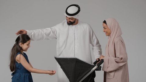 مفهوم الأسرة السعيدة ، بورتريه لسيدة عربية خليجية اماراتية ترتدي العباءة الملونه تقف برفقة طفلتها الصغيرة و زوجها و عربة الأطفال بإيماءات تدل على السعادة و المحبة و الحنان ، رابطة الأمومة ، ترابط عاطفي ، نزهة و جولة عائلية ، قضاء أوقات عائلية ممتعة