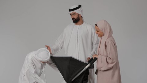 Spending quality time with children, strengthening the bonds of love and family cohesion, the concept of love, intimacy and family bonding, a portrait of an Emirati Gulf Arab child wearing traditional clothing gently and quietly caressing infants inside the stroller with his parents, gestures of happiness and pleasure