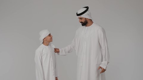 تقوية روابط المحبة والتماسك الأسري، مفهوم المحبة والألفة والترابط الأسري، قضاء وقت ممتع مع الابناء، بورتريه لاب عربي خليجي اماراتي يرتدي الكندورة و الغتره برفقه ابنه ينظر الى الكاميرا بايماءات السعادة و السرور