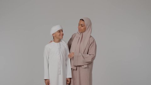 The concept of love, intimacy and family bonding, a pleasant family atmosphere, spending quality time with the children, a portrait of an Arab Gulf Emirati woman wearing a colorful abaya with her son looking at the camera with gestures of happiness and pleasure