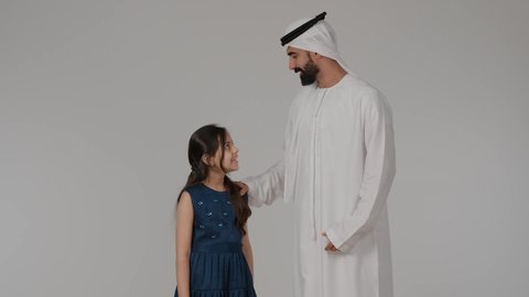 قضاء وقت ممتع مع الابناء، مفهوم المحبة والألفة والترابط الأسري، أجواء أسرية ممتعة، بورتريه لرجل عربي خليجي اماراتي يرتدي الكندورة و الغتره برفقه ابنته ينظرالى الكاميرا بايماءات السعادة و السرور