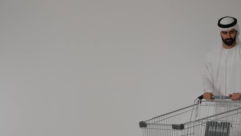 التجول وتبضع المستلزمات , الترابط الأسري والاستمتاع مع العائلة, قضاء الأوقات برفقة الأبناء، بورترية لرجل عربي خليجي اماراتي يرتدي الزي التقليدي يقوم بجر عربة التسوق برفقه ابنه ، الاستفاده من العروض والتخفيضات الموسميه