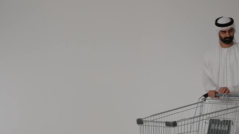 الاشارة إلى شيء ما بعيد والنظر إليه, الترابط الأسري والاستمتاع مع العائلة, قضاء الأوقات برفقة الأبناء، بورترية لرجل عربي خليجي اماراتي يرتدي الزي التقليدي يقوم بجر عربة التسوق برفقه ابنه ، الاستفاده من العروض والتخفيضات الموسميه