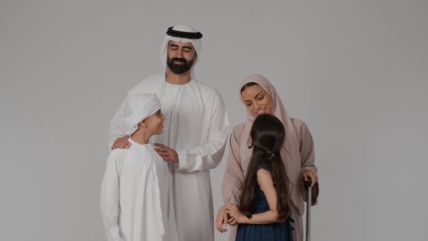 The concept of a close-knit and happy family, summer vacation tourism, a portrait of an Emirati Gulf Arab family wearing traditional clothing preparing for a fun and entertaining summer trip, a Gulf woman holding a travel bag in her hands with gestures of happiness and pleasure