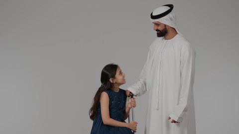 التجهيز للسفر و الرحلات الممتعة، السياحة في إجازة الصيف, الشعور بالسعادة والفرح, عائله عربيه خليجيه اماراتية تستعد لقضاء رحلة صيفية ممتعة, بورترية لرجل عربي خليجي اماراتي يرتدي الكندورة و الغتره يمسك بيده حقيبه السفر برفقه ابنته