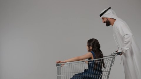 ايماءات السعادة و السرور، الاستفاده من العروض والتخفيضات الموسميه ، بورتريه لرجل عربي خليجي اماراتي يرتدي الكندورة و الغتره يقوم بالتبضع و شراء المستلزمات، بنت خليجيه اماراتية تجلس داخل عربة التسوق و تقوم بالاشارة الى شيء ما، التجول والترفيه ، أجواء عائلية سعيدة