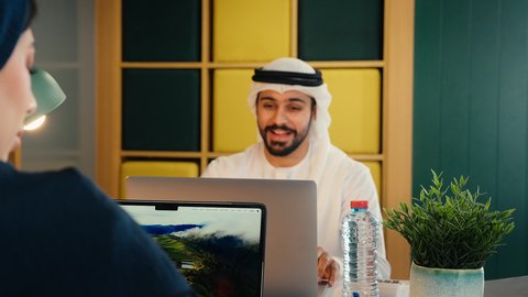 اجراء مكالمه عمل فيديو، استخدام التقنيات الحديثة والمتطورة، تصوير مقرب لرجل عربي خليجي اماراتي يرتدي الكندورة و الغتره يقوم بعمل اجتماع عن بعد عبر الحاسوب المحمول، اداء المهام للتطور المهني وتحقيق الاهداف