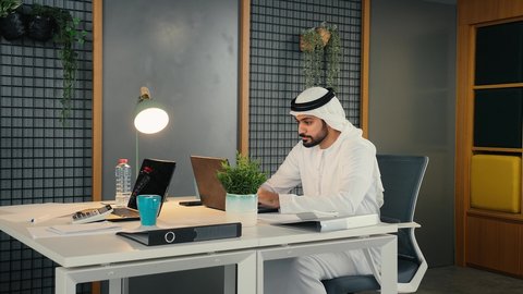 Developing strategic plans to achieve goals, the concept of collaborative management, an Emirati Gulf Arab man wearing a kandura and ghutra sitting inside the company headquarters, learning work methods and professional development, administrative office jobs and professions, equality between men and women, teamwork and team spirit