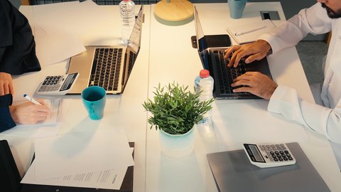 تدوين الملاحظات على الورق،مهن ووظائف ادارية مكتبية, استخدام الأجهزة التكنولوجية الحديثة والمتطورة، تصوير مقرب لرجل عربي خليجي اماراتي يرتدي الكندورة يجلس على مكتبه و يقوم بالكتابة على الحاسب المحمول