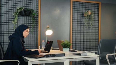 التوظيف في المكاتب والشركات الاماراتية، استخدام التقنيات الحديثة والتكنولوجيا بالمجال الإداري، امراة عربيه خليجيه اماراتيه ترتدي العباءة السوداء تجلس على المكتب وأمامها الحاسوب المحمول، رجل خليجي يقوم بتقديم كوب من المشروب الساخن لزميلته