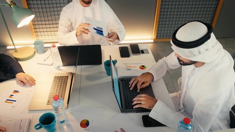 دراسة أوراق البيانات الإحصائية، دراسه وتحليل المشاريع الجديده ومناقشه اداء وتقارير العمل، إدارة مهام العمل اليومية في مقر الشركة، تطوير الخطط والاسترتيجيات، تصوير مقرب لرجلان عربيان خليجيان اماراتيان يرتديان الكندورة و الغتره يجلسان في المكتب يقومان بالعمل على جهاز الحاسوب المحمول