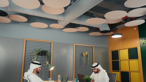 مهن ووظائف اماراتية، إدارة مهام العمل اليومية في مقر الشركة، تطوير الخطط والاسترتيجيات، استخدام الأجهزة التقنية الحديثة، رجلان عربيان خليجيان اماراتيان يرتديان الكندورة و الغتره يجلسان في المكتب يقومان بالعمل على جهاز الحاسوب المحمول