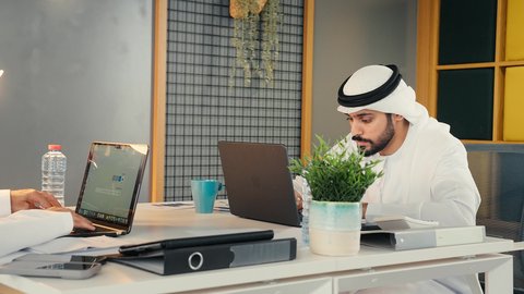 Developing plans and strategies, managing daily work tasks at the company's headquarters, Emirati professions and jobs, using modern technical devices, a close-up of an Emirati Gulf Arab man wearing a kandura and ghutra sitting in his office working on a laptop