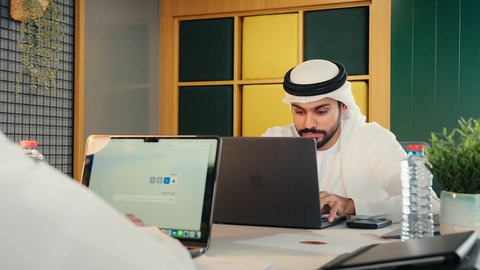 إدارة مهام العمل اليومية في مقر الشركة، مهن ووظائف اماراتية، استخدام الأجهزة التقنية الحديثة، تصوير مقرب لرجل عربي خليجي اماراتي يرتدي الكندورة و الغتره يجلس في مكتبه يعمل على جهاز الحاسوب المحمول، تطوير الخطط والاسترتيجيات، تعابير الكسل والخمول، الحاجة للنوم والراحة