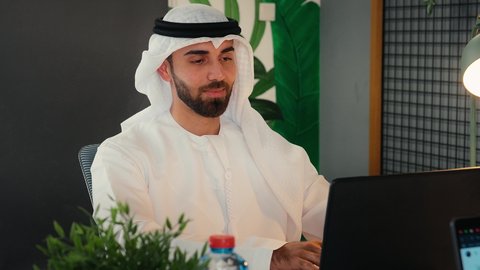 احتراف وظائف الحاسوب وتكنولوجيا المعلومات، تصوير مقرب لرجل عربي خليجي اماراتي يرتدي الزي التقليدي يجلس في مكتب العمل، استخدام جهاز الحاسوب المحمول، انجاز مهام العمل، تصفح الانترنت، اعمال مكتبية، مقر العمل، استخدام وسائل تقنية حديثة