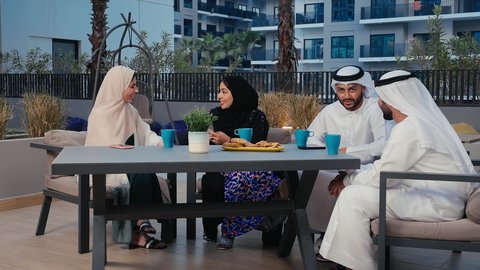 Youth friendships, fun and acquaintances, discussions and dialogues, Arab Gulf Emirati friends enjoying a good time in an Emirati cafe, an Arab Gulf Emirati woman wearing the hijab holding a mobile phone in her hand with gestures of happiness and pleasure