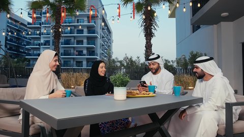 مطاعم و كافيهات في الإمارات، جلسات تعارف وديه، أصدقاء عرب خليجيين اماراتيين يستمتعون بتبادل الحديث في احد المقاهي الاماراتية ، التسامر والدردشة مع الأصدقاء، رجل عربي خليجي اماراتي يرتدي الكندورة و الغتره يمسك بيده الهاتف المحمول
