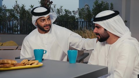 وناسة وتعارف وأجواء سعيدة، قضاء أوقات ممتعة،تصوير مقرب لرجلان عربيان خليجيان اماراتيان يرتديان الكندورة و الغتره  يستمتعان  بتبادل الحديث في احد المقاهي الاماراتية، المشروبات الباردة والأطعمة اللذيذة ، ديوانية اماراتية