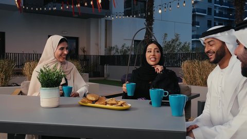 النقاش والحوار بين الاصدقاء ، قضاء أوقات ممتعة، رجلان عربيان خليجيان اماراتيان يرتديان الزي الاماراتي التقليدي و امراتان عربيتان اماراتيان يستمتعون بتبادل الحديث في احد المقاهي الاماراتية، المشروبات الباردة والأطعمة اللذيذة ، ديوانية اماراتية، وناسة وتعارف وأجواء سعيدة