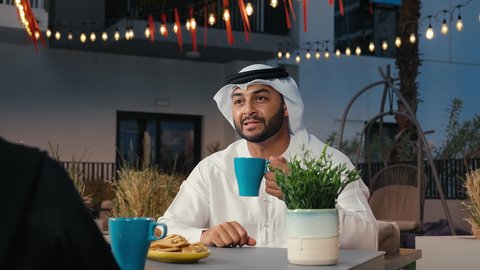 الاستمتاع بتناول المشروبات المفضلة، قضاء أوقات ممتعة في الهواء الطلق بأجواء لطيفة، الخروج في سهرة مسائية عائلية،تصوير مقرب لرجل عربي خليجي اماراتي يرتدي الكندورة و الغتره يجلس فى احدي المقاهي فى الامارات العربية ، نقاشات و حوارات عائليه