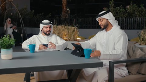 قضاء وقت ممتع مع الأصدقاء في عطلة نهاية الأسبوع، تبادل الأفكار وبناء علاقات اجتماعية, الاستمتاع في التحدث والنقاش في إحدى المقاهي الفاخرة في الامارات, زملاء عمل عرب خليجيون اماراتيون في اجتماع عمل خارج الشركة يقومان بمشاهده التابلت ، الاستمتاع بتناول المشروبات