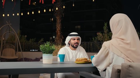 ايماءات تدل على السعادة والاستمتاع بالتحدث، مفهوم الرابطة الزوجية والألفة بين الزوجين، تصوير مقرب لزوجان عربيان خليجيان امارتيان يرتديان الزي التقليدي يجلسان فى احد المقاهي ، تناول المشروبات الباردة، نقاشات وحوارات، قضاء أوقات ممتعة