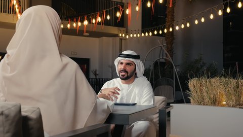 تبادل الأحاديث و الأخبار، مفهوم الرابطة الزوجية والألفة بين الزوجين، زوجان عربيان خليجيان امارتيان يرتديان الزي التقليدي يجلسان فى احد المقاهي ، تناول المشروبات الباردة، نقاشات وحوارات، قضاء أوقات ممتعة، أجواء عائلية سعيدة