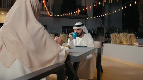 مفهوم الرابطة الزوجية والألفة بين الزوجين، زوجان عربيان خليجيان امارتيان يرتديان الزي التقليدي يستمتعان بتبادل الحديث في احد المقاهي ، تناول المشروبات الباردة، نقاشات وحوارات، قضاء أوقات ممتعة، أجواء عائلية سعيدة