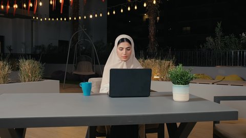 Using modern and advanced technical devices to complete projects in the cafe, completing work tasks remotely via the Internet, a close-up of a young Arab Gulf Emirati woman working on a laptop with gestures of integration and concentration, a Saudi woman sitting in a cafe in the United Arab Emirates