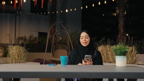الاستمتاع بتناول المشروبات ، إجراء مكالمة هاتفيه عبر الجوال , التواصل مع العائلة و الأصدقاء في أوقات الفراغ ، مشاركة الأخبار والأحاديث، امراه عربيه خليجيه اماراتية ترتدي العباءة  تستمع بقضاء وقت ممتع فى المطعم، سيده سعودية تمسك بيدها الهاتف المحمول بايماءات السعادة و السرور