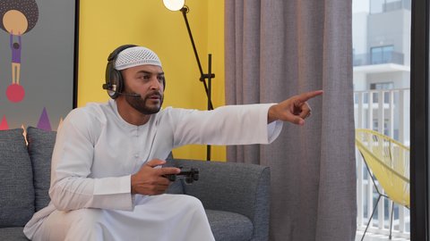 قضاء اوقات ممتعه ، تعابير الاندماج والتفاعل ، دمج التقنيات الحديثه فى المتعة والتسلية ، رجل عربي اماراتي خليجي يرتدي الكندورة والطاقيه وسماعات الرأس ، يمسك عصا التحكم ، ألعاب الفيديو الترفيهية