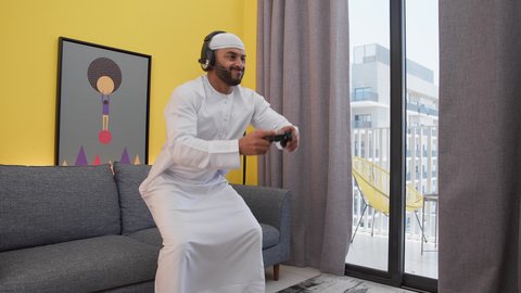 ألعاب الفيديو الترفيهية، ايماءات الهزيمة والغضب ، تعابير التحدى والخساره، دمج التقنيات الحديثه فى المتعة والتسلية ، قضاء اوقات ممتعه ، رجل عربي اماراتي خليجي يرتدي الكندورة والطاقيه وسماعات الرأس ، يمسك عصا التحكم