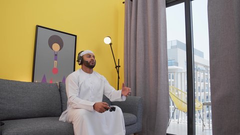 ألعاب الفيديو الترفيهية، رفع اليد بتعابير الخسارة، دمج التقنيات الحديثه فى المتعة والتسلية ، رجل عربي اماراتي خليجي يرتدي الكندورة والطاقيه وسماعات الرأس ، يمسكان عصا التحكم ، قضاء اوقات ممتعه