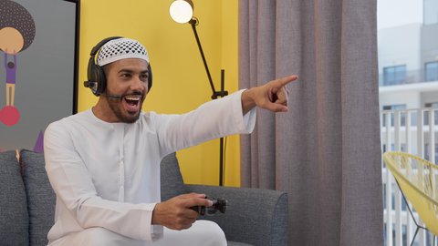 ألعاب الفيديو الترفيهية، تعابير السرور والسعادة بالانتصار ، رجل عربي اماراتي خليجي يرتدي الكندورة والطاقيه وسماعات الرأس ، يمسكان عصا التحكم ، قضاء اوقات ممتعه ، دمج التقنيات الحديثه فى المتعة والتسلية