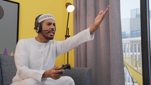 تعابير الخساره والهزيمه، دمج التقنيات الحديثه فى المتعة والتسلية ، ألعاب الفيديو الترفيهية، رجل عربي اماراتي خليجي يرتدي الكندورة والطاقيه وسماعات الرأس ، يمسكان عصا التحكم ، قضاء اوقات ممتعه