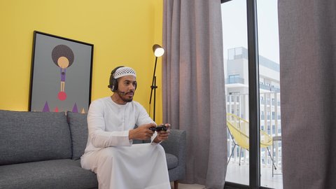 تعابير الفوز والانتصار، رجل عربي اماراتي خليجي يرتدي الكندورة والطاقيه وسماعات الرأس ، يمسكان عصا التحكم ، دمج التقنيات الحديثه فى المتعة والتسلية ، ألعاب الفيديو الترفيهية، قضاء اوقات ممتعه