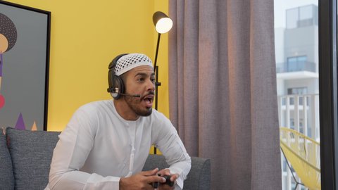 Having a good time, expressions of victory and triumph, an Emirati Arab Gulf man wearing a kandura, a taqiyah and headphones, holding a joystick, integrating modern technology into fun and entertainment, entertainment video games