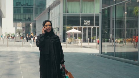 شراء الملابس و الاكسسوارات النسائيه ، عباءات خليجيه نسائيه عصريه، مفهوم التصوير والشهره عبر مواقع التواصل الاجتماعي،  تصوير لشابة عربية خليجية اماراتية ترتدي العباءة والحجاب ، تحمل اكياس التسوق ، سيدة سعودية تستمتع بمتعة الشراء