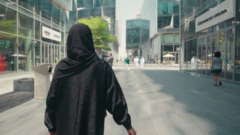 Taking advantage of seasonal discounts, a Saudi woman enjoying the pleasure of shopping, modern Gulf women's abayas, interest in fashion, beauty and elegance, buying women's clothes and accessories, a photo from the back of a young Arab Gulf Emirati woman wearing an abaya and hijab, carrying shopping bags