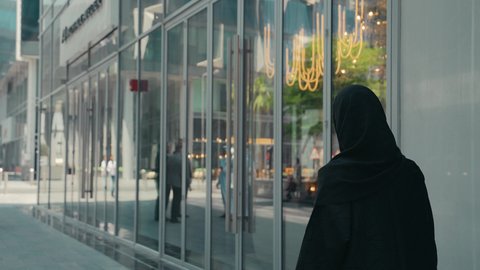 Interest in fashion, beauty and elegance, buying women's clothes and accessories, a photo from the back of a young Arab Gulf Emirati woman wearing an abaya and hijab, carrying shopping bags, taking advantage of seasonal discounts, modern Gulf women's abayas, a Saudi woman enjoying the pleasure of shopping