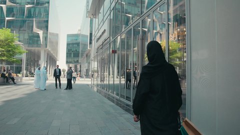 شراء الملابس و الاكسسوارات النسائيه ، تصوير من الخلف لشابة عربية خليجية اماراتية ترتدي العباءة والحجاب ، تحمل اكياس التسوق ، الاستفادة من التخفيضات الموسمية، عباءات خليجيه نسائيه عصريه، الإهتمام بالموضة والجمال والأناقة، سيدة سعودية تستمتع بمتعة الشراء