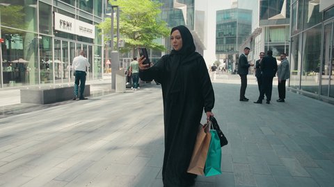 مفهوم التصوير والشهره عبر مواقع التواصل الاجتماعي، تصوير لشابة عربية خليجية اماراتية ترتدي العباءة والحجاب ، تحمل اكياس التسوق ، شراء الملابس و الاكسسوارات النسائيه ، عباءات خليجيه نسائيه عصريه، سيدة سعودية تستمتع بمتعة الشراء