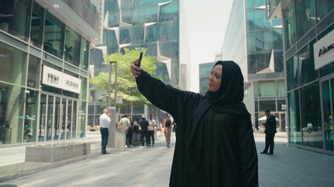 توثيق اللحظات السعيدة، استخدام الهاتف المحمول والتقنيات الحديثه، اجراء مكالمة فيديو ، امرأة عربية خليجية سعودية ترتدي العباءة والحجاب، سيدة اماراتية تنظر بتعابير السرور تقوم باستخدام الهاتف المحمول ، نزهة وجولة فى الهواء الطلق